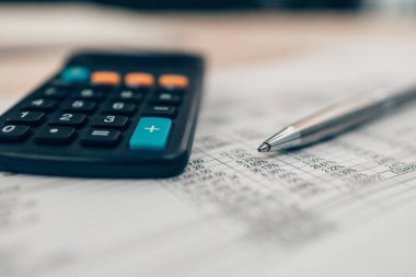 Masa başında kalem ve hesap makinesi var. Hesap makinesinin denge, projeksiyon, para ve maliyeti hesaplaması için nesne. Muhasebe ve Finans kavramı.