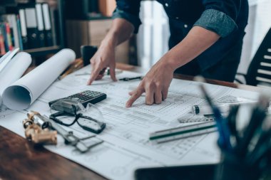 Engineering working with drawings inspection on the office desk and Calculator, triangle ruler, safety glasses, compass, vernier caliper on Blueprint. Engineer, Architect, Industry and factory concept.