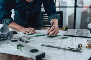 Engineering working with drawings inspection and writing on the office desk and Calculator, triangle ruler, safety glasses, compass, vernier caliper on Blueprint. Engineer, Architect, Industry and factory concept.