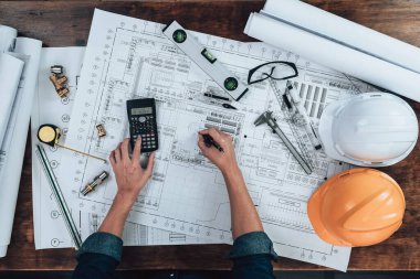 Üst Manzara Mühendisliği, çizim teftişi ve hesap makinesiyle çalışıyor. Ofis masasında ve üçgen cetvel, güvenlik gözlükleri, pusula, mavi çizimde vernier kalibre. Mühendis, Mimar, Endüstri ve Fabrika Konsepti.