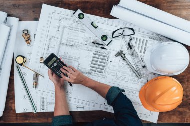 Top view Engineering working with drawings inspection and press calculator on the office desk and triangle ruler, safety glasses, compass, vernier caliper on Blueprint. Engineer, Architect, Industry and factory concept.
