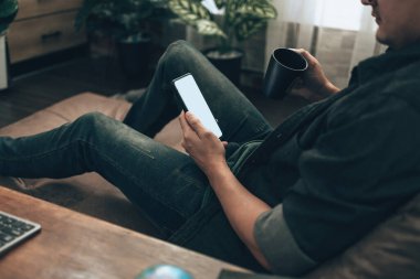 Erkekler cep telefonlarıyla el ele tutuşup evdeki kanepenin üzerinde boş ekranla mesajlaşıyorlar. Rahat ev kavramı.