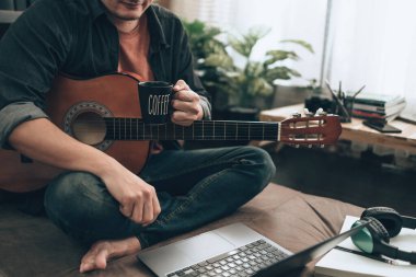 Genç adam evdeki oturma odasında kanepede otururken rahatlayıp gitar çalıyor. Müzik melodi, dizüstü bilgisayarda sözler ve pratik konsepti yaratır.