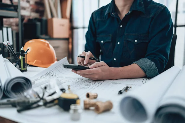 Engineering working with drawings inspection and press calculator on the office desk and triangle ruler, safety glasses, compass, vernier caliper on Blueprint. Engineer, Architect, Industry and factory concept.