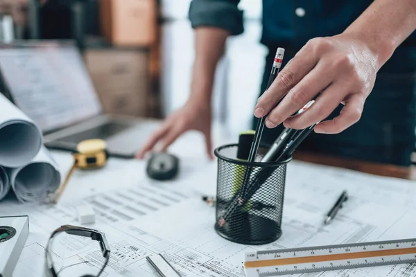 Engineering pick pencil from pencil case for drawings inspection on the office desk and Calculator, triangle ruler, safety glasses, compass, vernier caliper on Blueprint. Engineer, Architect, Industry and factory concept.