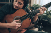 mladý muž relaxovat a hrát na kytaru, zatímco sedí na pohovce v obývacím pokoji doma. 