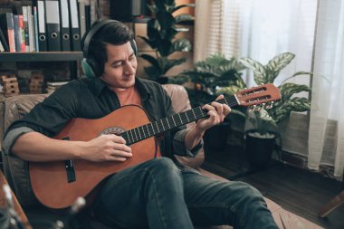Genç adam evdeki oturma odasında kanepede otururken rahatlayıp gitar çalıyor.. 