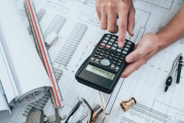 Mühendislik büro masasında çizim teftişi ve basın hesap makinesi ile çalışıyor. Üçgen cetvel, güvenlik gözlükleri, pusula, mavi planda vernier kalibre. Mühendis, Mimar, Endüstri ve Fabrika Konsepti.