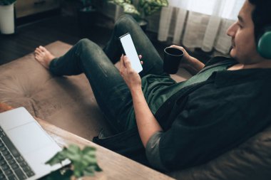 Erkekler cep telefonlarıyla el ele tutuşup evdeki kanepenin üzerinde boş ekranla mesajlaşıyorlar. Rahat ev kavramı.