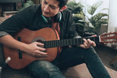 Genç adam evdeki oturma odasında kanepede otururken rahatlayıp gitar çalıyor.. 