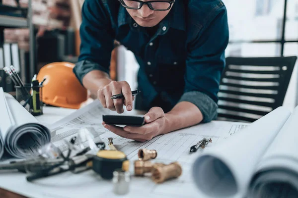 Engineering working with drawings inspection and press calculator on the office desk and triangle ruler, safety glasses, compass, vernier caliper on Blueprint. Engineer, Architect, Industry and factory concept.