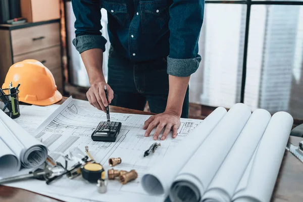 Engineering working with drawings inspection and press calculator on the office desk and triangle ruler, safety glasses, compass, vernier caliper on Blueprint. Engineer, Architect, Industry and factory concept.