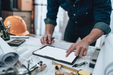 Mühendislik, ofisteki tablet ve hesap makinesi, üçgen cetvel, güvenlik gözlüğü, pusula üzerinde çizim teftişi ile çalışıyor. Mühendis, Mimar, Endüstri ve Fabrika Konsepti.