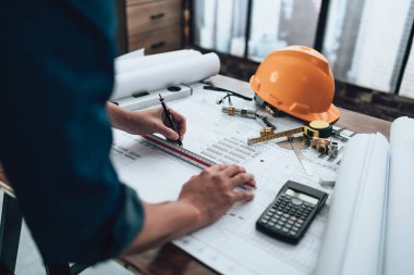 Engineering working with drawings inspection and writing on the office desk and Calculator, triangle ruler, safety glasses, compass, vernier caliper on Blueprint. Engineer, Architect, Industry and factory concept.