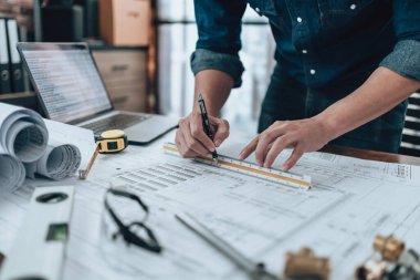 Engineering working with drawings inspection and writing on the office desk and Calculator, triangle ruler, safety glasses, compass, vernier caliper on Blueprint. Engineer, Architect, Industry and factory concept.