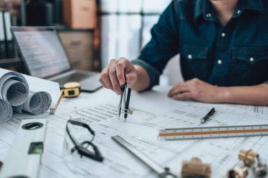 Engineering working with drawings inspection and writing on the office desk and Calculator, triangle ruler, safety glasses, compass, vernier caliper on Blueprint. Engineer, Architect, Industry and factory concept.