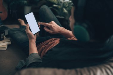 Erkekler cep telefonlarını boş ekran ile tutuyorlar ve evdeki koltukta kulaklık takıyorlar. Rahat ev kavramı.