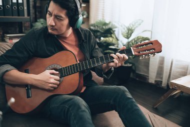 Genç adam evdeki oturma odasında kanepede otururken rahatlayıp gitar çalıyor.. 