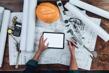 Mühendislik, ofisteki tablet ve hesap makinesi, üçgen cetvel, güvenlik gözlüğü, pusula üzerinde çizim teftişi ile çalışıyor. Mühendis, Mimar, Endüstri ve Fabrika Konsepti.