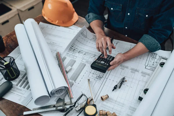 Engineering working with drawings inspection and press calculator on the office desk and triangle ruler, safety glasses, compass, vernier caliper on Blueprint. Engineer, Architect, Industry and factory concept.