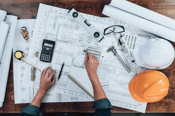 Top view Engineering working with drawings inspection and writing on the office desk and Calculator, triangle ruler, safety glasses, compass, vernier caliper on Blueprint. Engineer, Architect, Industry and factory concept.