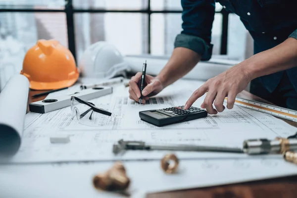 Engineering working with drawings inspection and writing on the office desk and Calculator, triangle ruler, safety glasses, compass, vernier caliper on Blueprint. Engineer, Architect, Industry and factory concept.