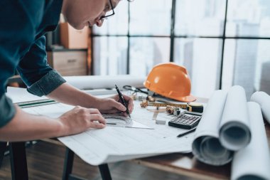 Engineering working with drawings inspection and writing on the office desk and Calculator, triangle ruler, safety glasses, compass, vernier caliper on Blueprint. Engineer, Architect, Industry and factory concept.