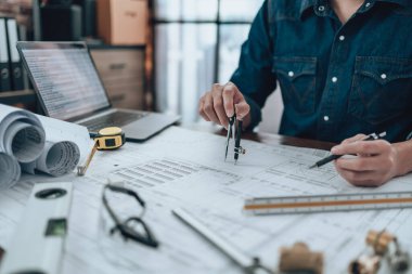 Engineering working with drawings inspection and writing on the office desk and Calculator, triangle ruler, safety glasses, compass, vernier caliper on Blueprint. Engineer, Architect, Industry and factory concept.