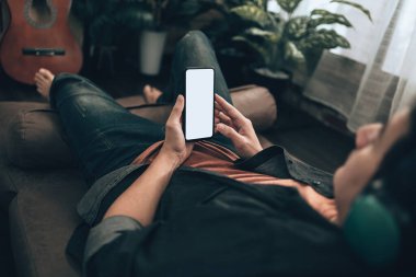 Erkekler cep telefonlarını boş ekran ile tutuyorlar ve evdeki koltukta kulaklık takıyorlar. Rahat ev kavramı.