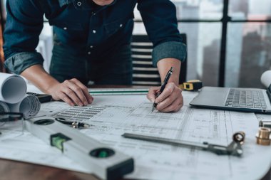 Engineering working with drawings inspection and writing on the office desk and Calculator, triangle ruler, safety glasses, compass, vernier caliper on Blueprint. Engineer, Architect, Industry and factory concept.