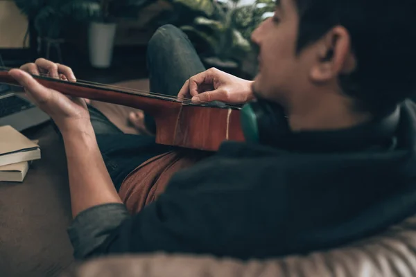 Νεαρός Άνδρας Χαλαρώστε Και Παίζοντας Κιθάρα Ενώ Κάθεται Στον Καναπέ — Φωτογραφία Αρχείου