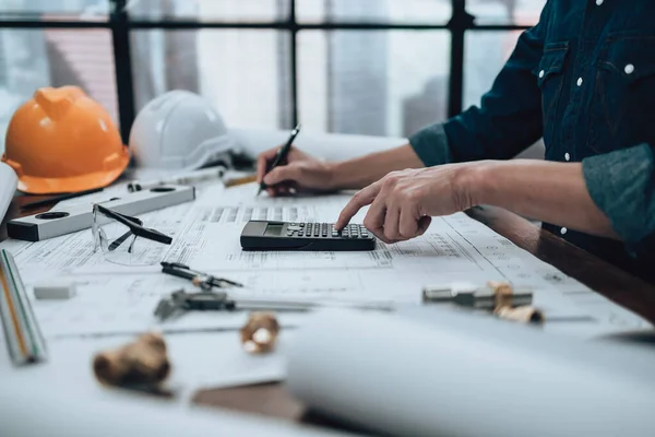 Engineering working with drawings inspection and press calculator on the office desk and triangle ruler, safety glasses, compass, vernier caliper on Blueprint. Engineer, Architect, Industry and factory concept.