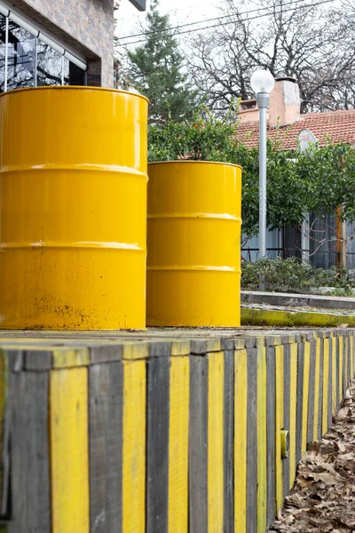 Yellow barrels on a wooden fence in the street. Yellow barrels of oil on the background of a row of yellow and black fences.