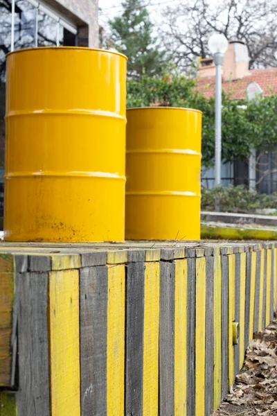 Yellow barrels on a wooden fence in the street. Yellow barrels of oil on the background of a row of yellow and black fences.