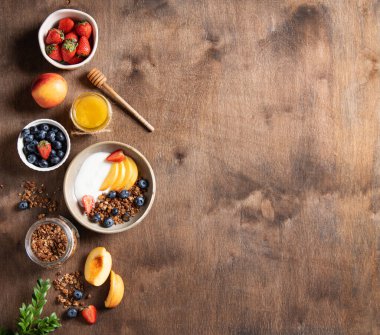 Ev yapımı granola, şeftali, böğürtlen ve bal ile birlikte koyu ahşap bir arka planda lezzetli bir yoğurt yatıyordu. Sağlıklı ve besleyici kahvaltı kavramı. Üst görünüm ve uzayın kopyası..