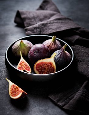 Koyu gri arka planda siyah bir kasede taze incir. Sağlıklı yemek kavramı. Makro ve yakın görünüm.