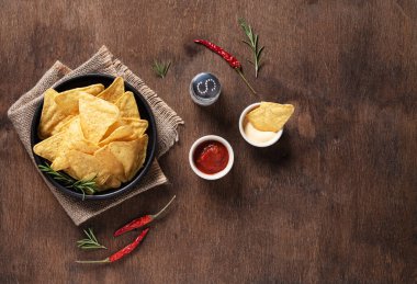 Geleneksel Meksika mısır cipsleri, salsa ve krema soslu nachos, otlar, ahşap arka planda tuz ve kırmızı biber ile yassılaşmış. Üst görünüm ve kopyalama alanı.