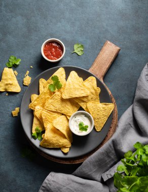 Geleneksel Meksika yemeği. Mısır cipsi, salsa soslu ve peynirli nachos ve koyu arkaplanda gri tabakta taze bitki. en üstteki görünüm ve kopyala. 