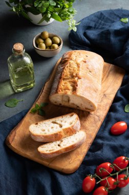 İtalyan ciabatta ekmeği domatesli, fesleğenli ve zeytinli dilimler koyu arka planda. Üst görünüm.