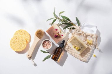 Doğal kozmetik ürünlerle bembeyaz güzellik spa 'sı: doğal sabun, sünger, mineral tuzu, yağ ve masaj fırçaları sert gölgeli beyaz arka planda. Çevre dostu ve sıfır atık konsepti. Üst görünüm.