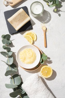 Düz sarı deniz tuzu, limon, sabun, havlu, fırça ve okaliptüs dallarıyla bembeyaz bir arka planda yatıyordu. Spa ve sağlık konsepti. Üst görünüm.