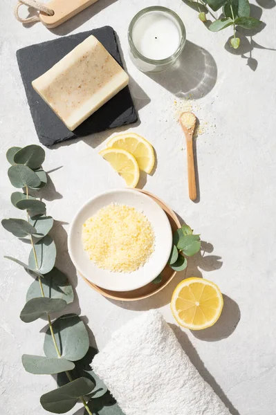Düz sarı deniz tuzu, limon, sabun, havlu, fırça ve okaliptüs dallarıyla bembeyaz bir arka planda yatıyordu. Spa ve sağlık konsepti. Üst görünüm.