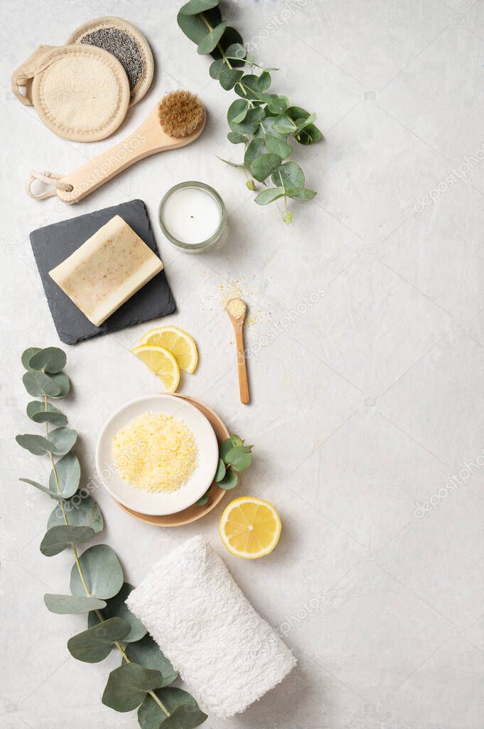 Flat lay organic yellow sea salt with lemon,  soap,  brush, sponge and eucalyptus branch  on a white textured background. The concept of spa and wellness. Top view and copy space