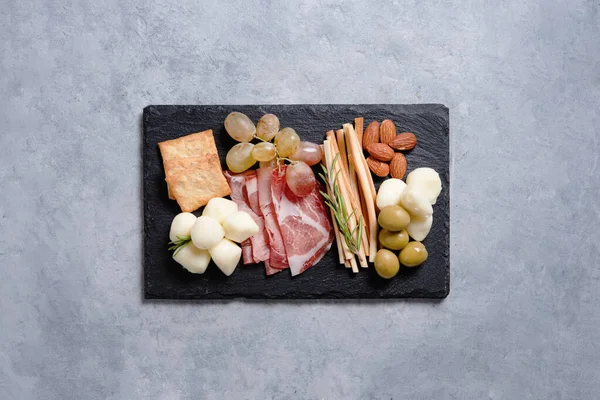 青い背景の黒い石板にチーズ モッツァレラチーズ オリーブ ナッツ ブドウ その他の軽食が付いたプレート イタリア料理のコンセプト トップ表示とコピースペース — ストック写真