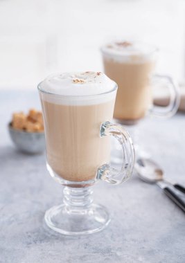 Two glasses of fragrant cappuccino coffee with cinnamon on a blue table against the background of a white kitchen in the early morning. Breakfast concept. Front view and close up.