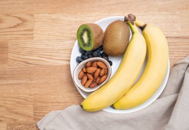 Üzerinde muz, kivi, böğürtlen ve fındık olan bir tabak. Sağlıklı beslenme kavramı. Beslenme ürünleri. Üst görünüm, metin için boş alan.