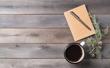 Eski ahşap arka planda köknar dalı olan bir fincan sade kahve ve el işi not defteri. Doğal malzemeler, seyahat planlama, ev ve iş yeri kavramı. Üst görünüm ve kopyalama alanı