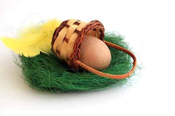 Пасхальное яйцо в пасхальной корзине с желтым пером — стоковое фото