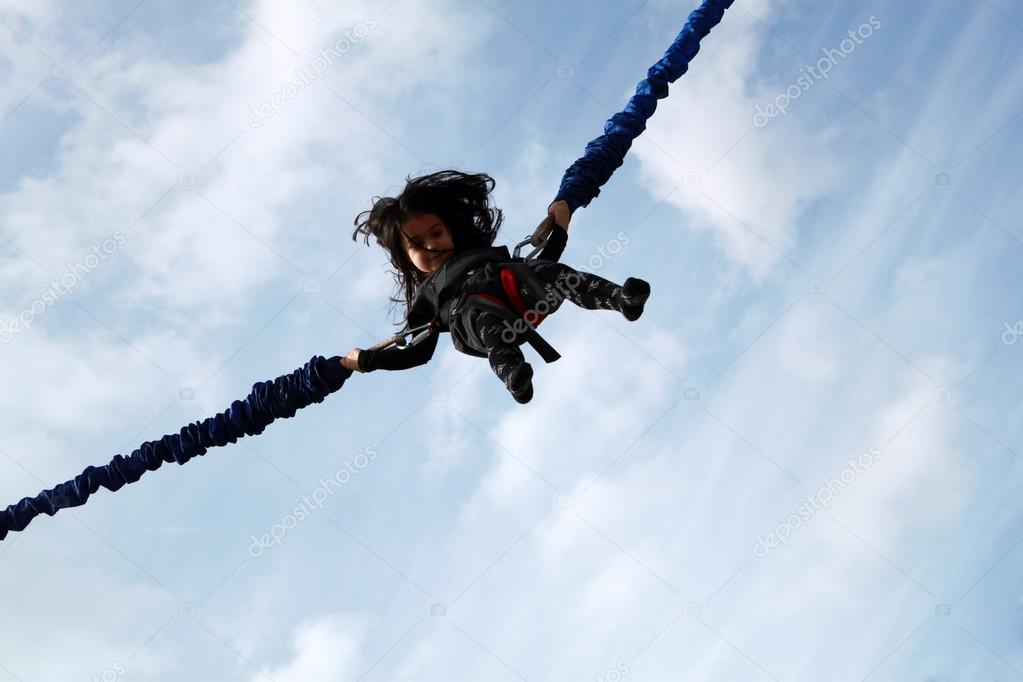 Little girl jumping on bungee on blue sky background