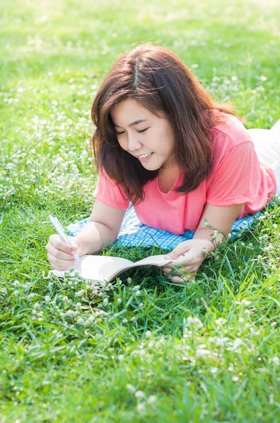 Glad ung asiatisk kvinna skriver i anteckningsboken och ler — Stockfoto